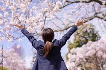 桜の木下で両手を上げる新入社員の女性